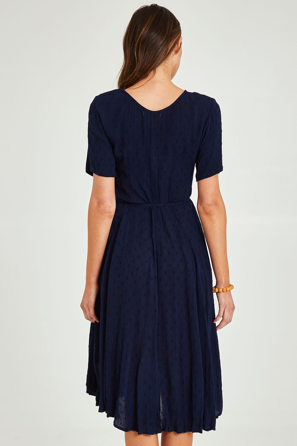 Model Madeline wearing size 10 of the Essentials Godet Short Sleeve Dress in colour Navy (Blue), from the back