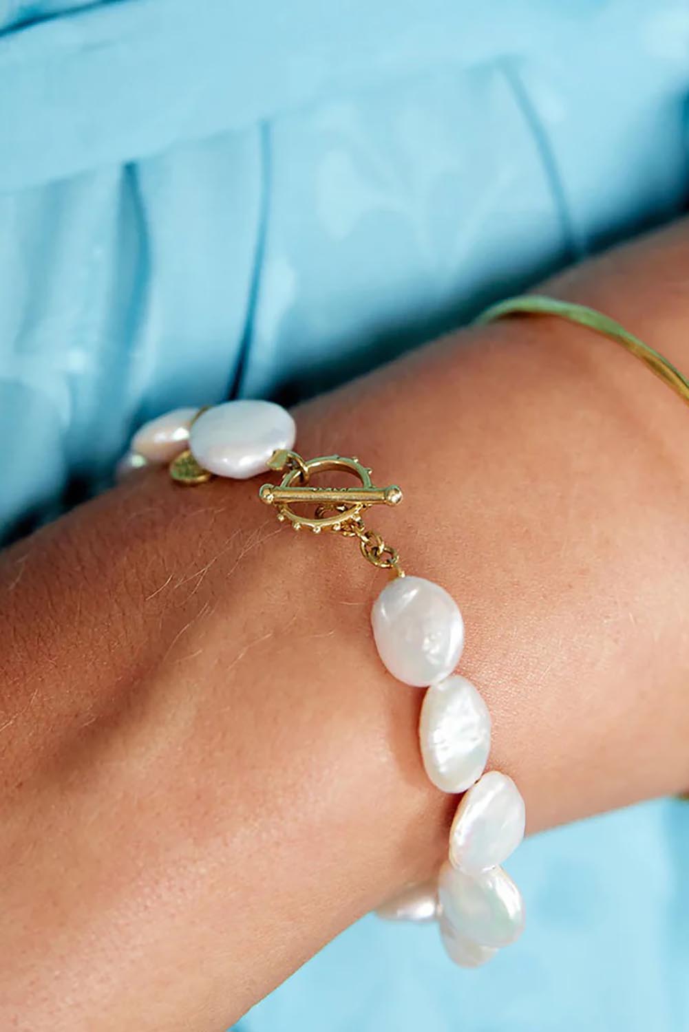 A model wearing the Pearl Fob Bracelet in colour Pearl (White), from the front, cropped image