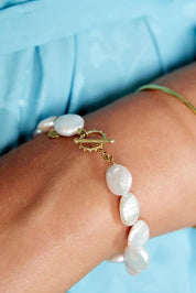 A model wearing the Pearl Fob Bracelet in colour Pearl (White), from the front, cropped image