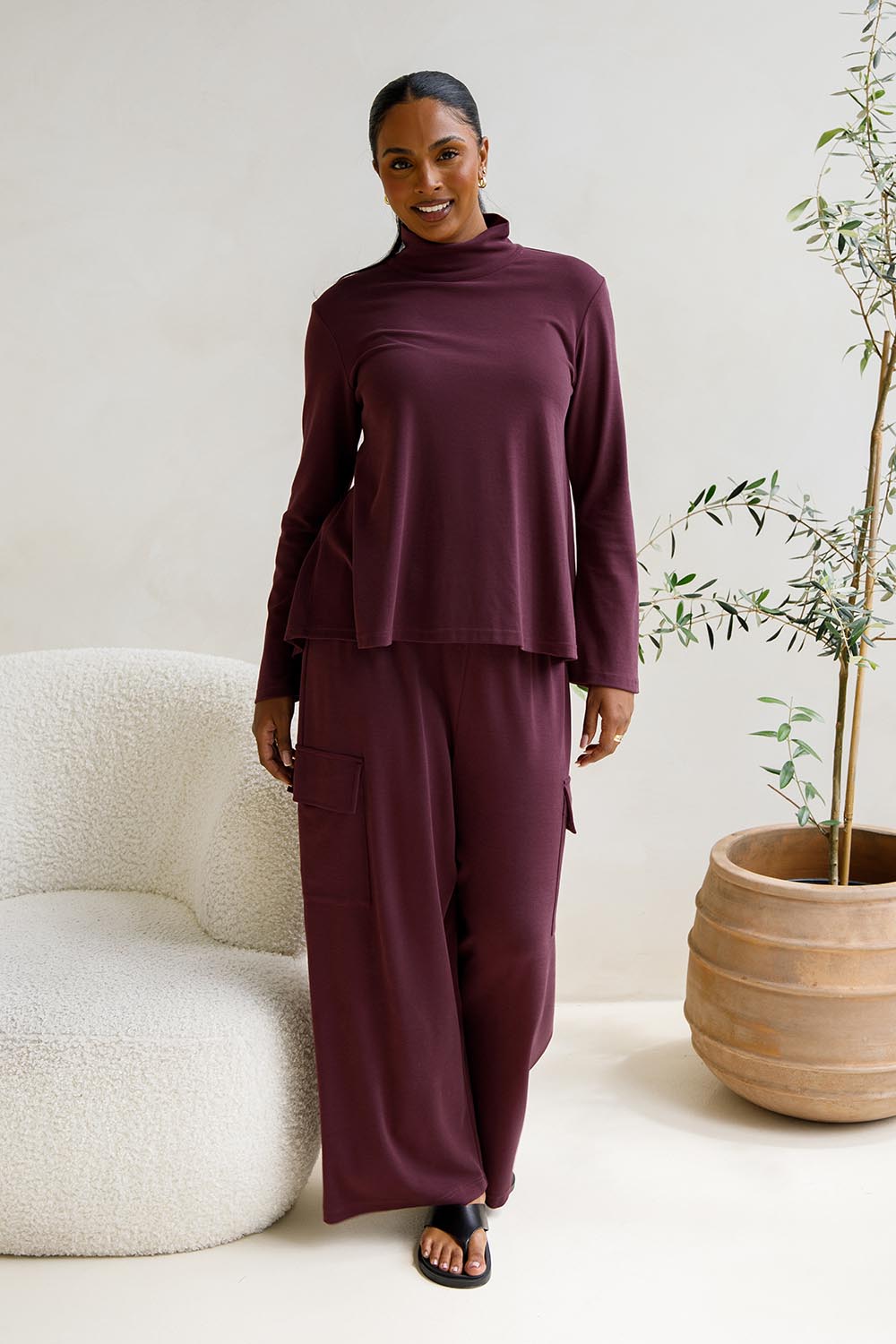 A model wearing the Eden Cotton Blend Pants in colour Plum (Red), from the front, showing the whole outfit