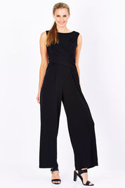 Model Maddy wearing size 10 of The Cross Waist Jumpsuit in colour Black (Black), from the front, showing the whole outfit