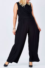 Model Natalie wearing size 16 of The Cross Waist Jumpsuit in colour Black (Black), from the front, cropped image