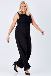 Model Natalie wearing size 16 of The Cross Waist Jumpsuit in colour Black (Black), from the front, showing the whole outfit