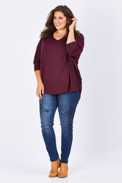 Model Mae wearing size 18 of The V Neck Side Drape Tee in colour Wine (Purple), from the front, showing the whole outfit