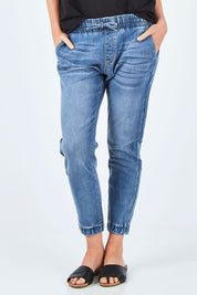 Model Chelsea wearing size 10 of The Pull On Jogger Jean in colour Denim (Blue), from the front, cropped image