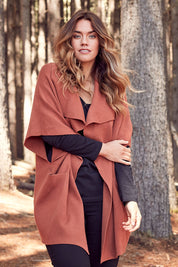 Model Laura wearing size OneSize of The Oversized Cape in colour Rust, from the front, showing the whole outfit