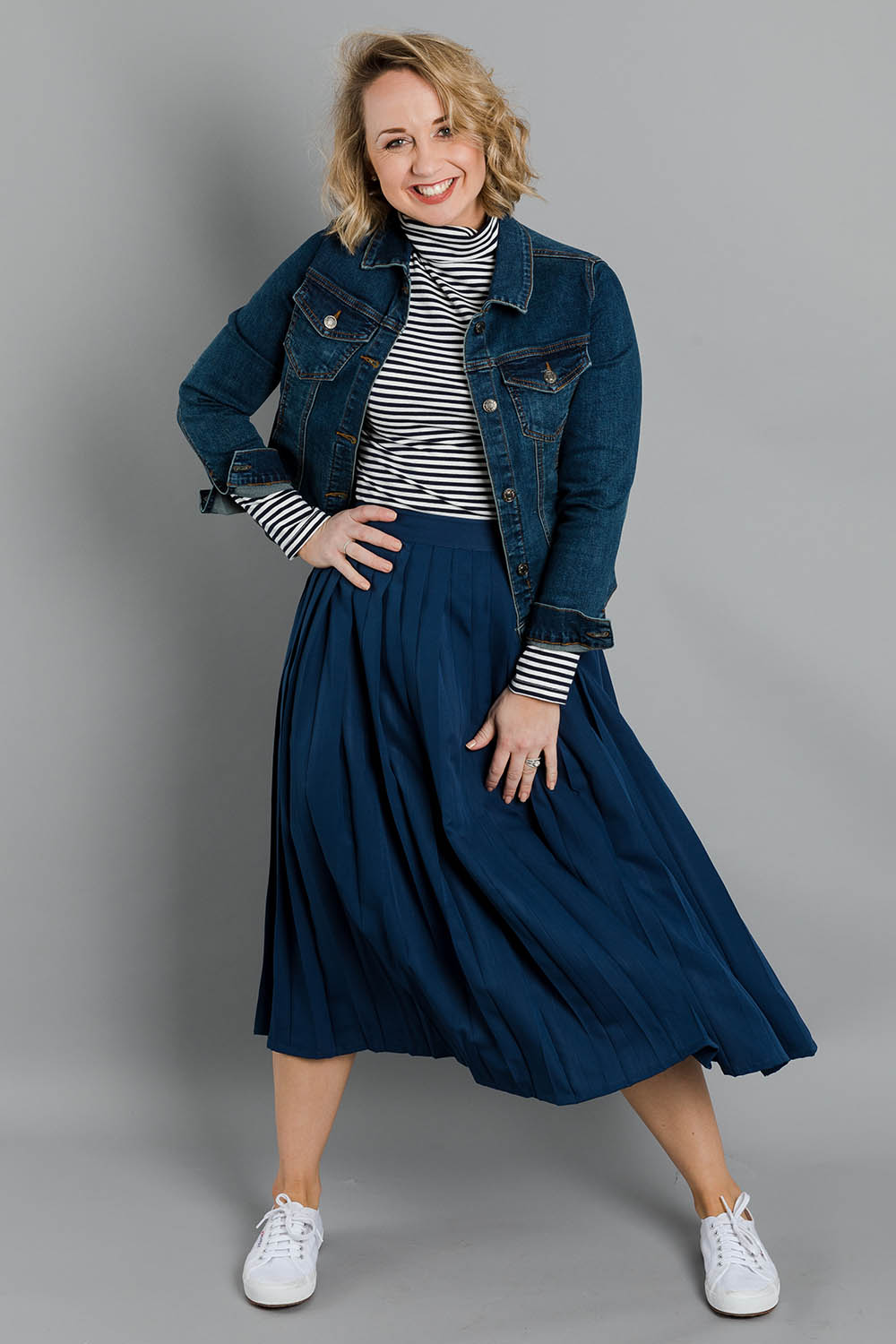 Model Steph wearing size 10 of The Pleated Skirt in colour Navy (Blue), from the front, showing the whole outfit