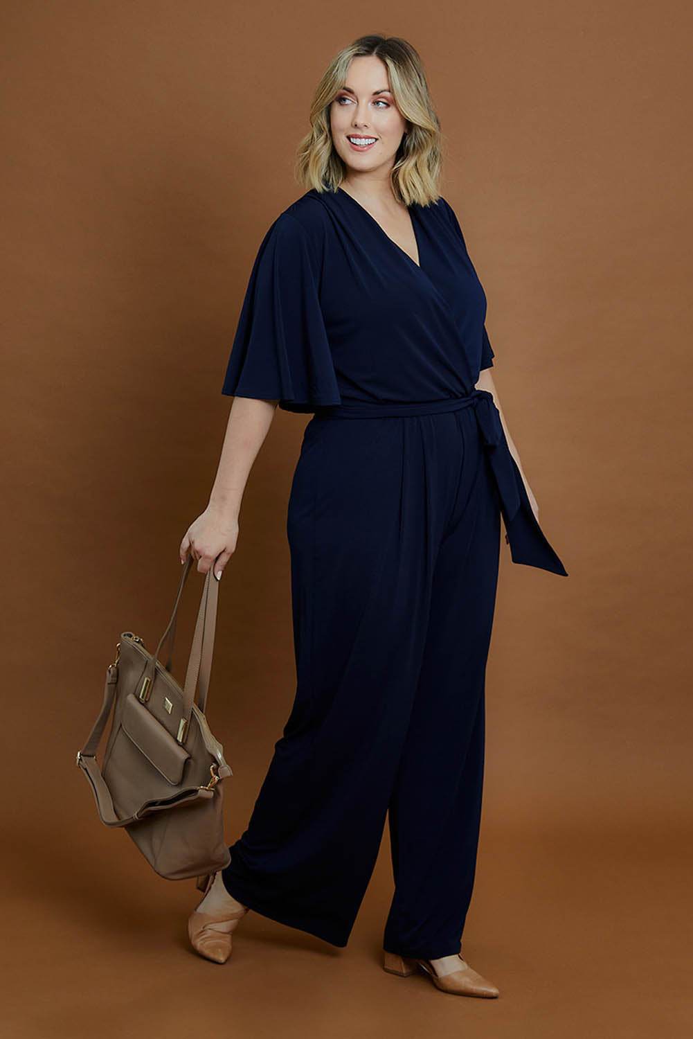 Model Jess wearing size 14 of The Bell Sleeve Jumpsuit in colour Navy (Blue), from the front, showing the whole outfit