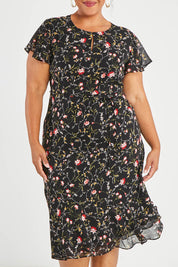 Model Alexis wearing size 16 of The Printed Chiffon Lined Dress in colour Botanical (Black), from the front, cropped image