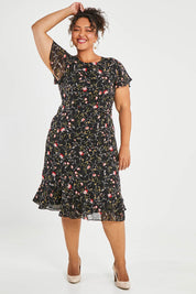 Model Alexis wearing size 16 of The Printed Chiffon Lined Dress in colour Botanical (Black), from the front, showing the whole outfit
