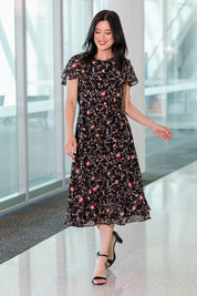 Model Miranda wearing size 10 of The Printed Chiffon Lined Dress in colour Botanical (Black), from the front, showing the whole outfit