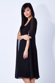 Model Miranda wearing size 10 of the Belle Cape Dress in colour Black (Black), from the front, cropped image