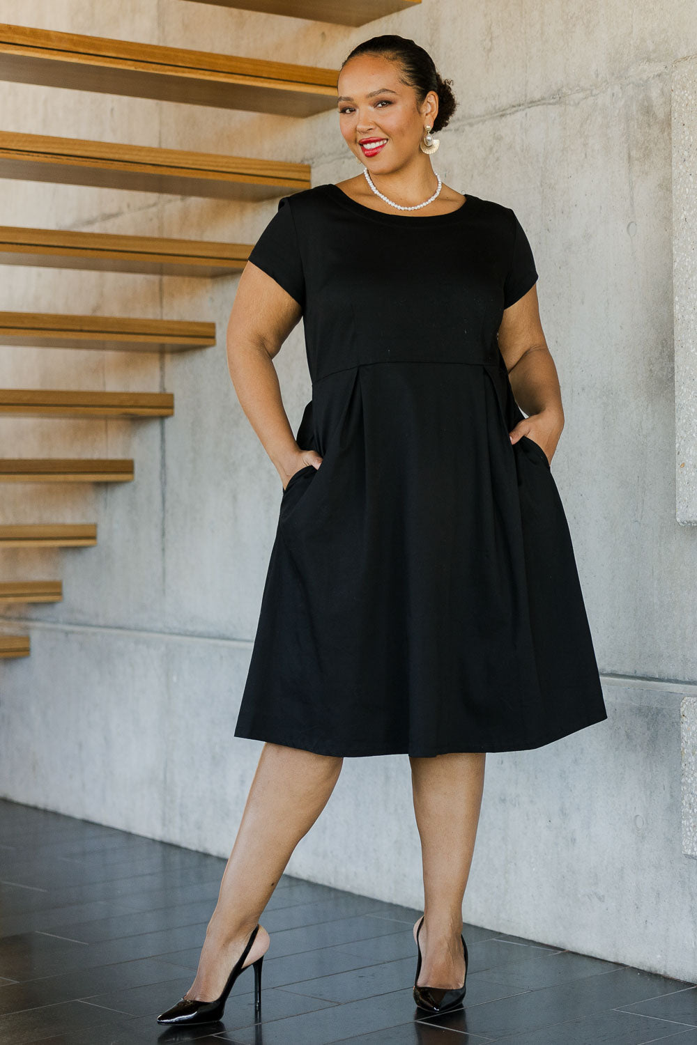 Model Alexis wearing size 18 of the Belle Cotton Sateen Pleat Dress in colour Black (Black), from the front, showing the whole outfit