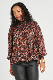 Model Noli wearing size 14 of the Romance In The Air Blouse in colour Blkrust (Black), from the front, cropped image