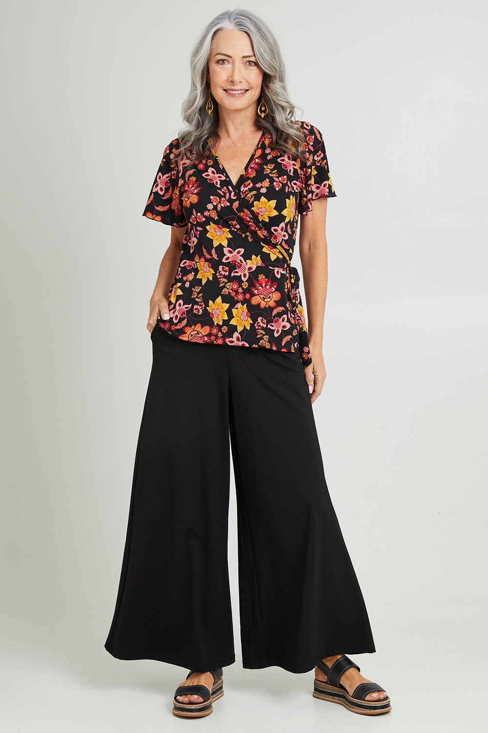 Model Luisa wearing size 10 of the All For You Wrap Top in colour Blkfleur (Black), from the front, showing the whole outfit