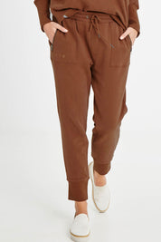 Model Madeline wearing size 10 of the Fundamentals Cosy Track Pant in colour Choc, from the front, cropped image