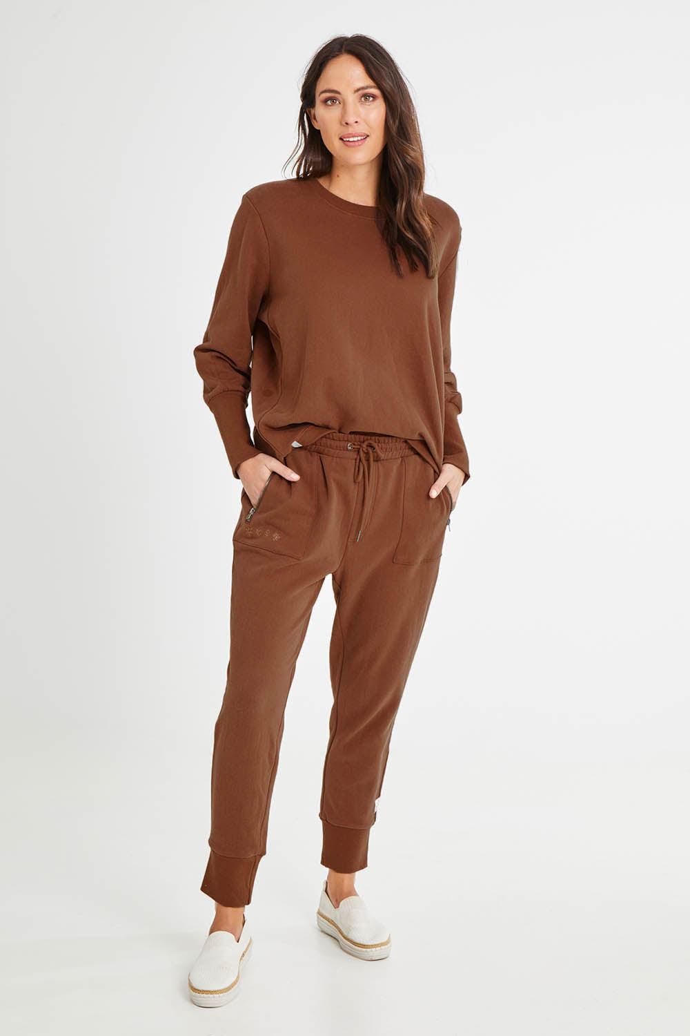 Model Madeline wearing size 10 of the Fundamentals Cosy Track Pant in colour Choc, from the front, showing the whole outfit