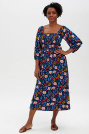 A model wearing the Raquel Shirred Dress in colour Blue (Blue), from the front, showing the whole outfit