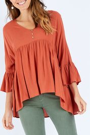Model Madeline wearing size S of the Ruffle Hem Top in colour Brick (Red), from the front, cropped image
