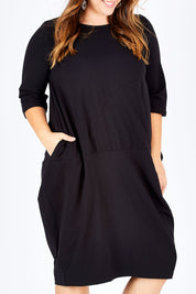 Model Sophie wearing size L of the Curved Seam Dress in colour Black (Black), from the front, cropped image