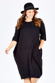 Model Sophie wearing size L of the Curved Seam Dress in colour Black (Black), from the front, cropped image