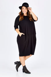 Model Sophie wearing size L of the Curved Seam Dress in colour Black (Black), from the front, showing the whole outfit