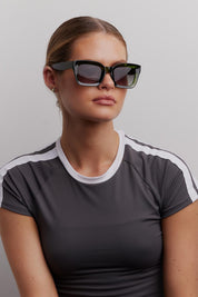 A model wearing the Onassis Polarized Square Sunglasses in colour Mossgreen (Green), from the front, cropped image