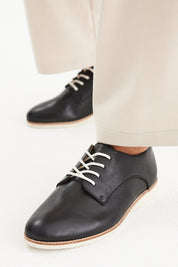 A model wearing the Classic Derby Flat in colour Black (Black), from the front, showing the whole outfit