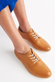 A model wearing the Classic Derby Flat in colour Cognac, from the front, showing the whole outfit