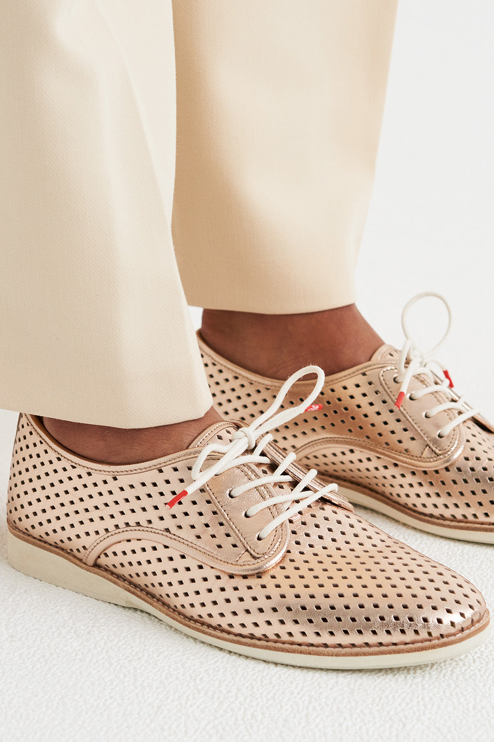 A model wearing the Derby Punch Metallic Flat in colour Rosegold (Metallics), from the front, showing the whole outfit