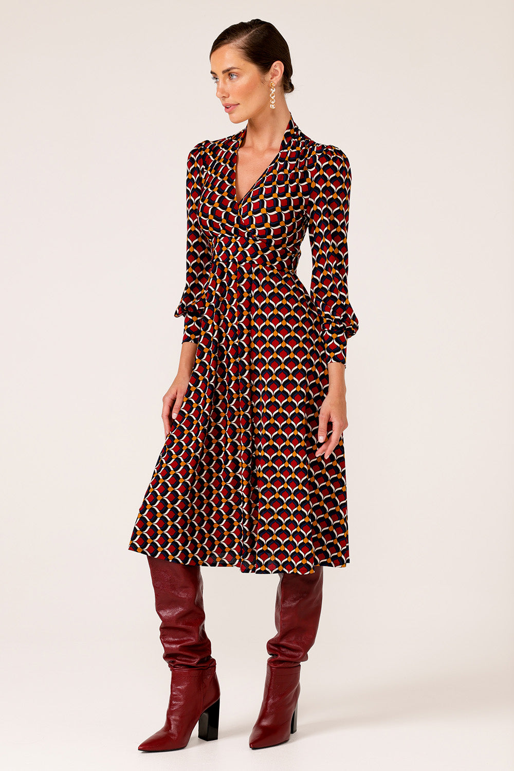 A model wearing the Auriga Dress in colour Ruby (Red), from the front, showing the whole outfit