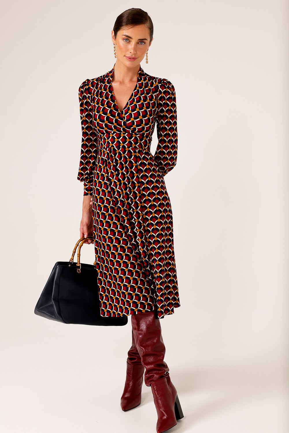 A model wearing the Auriga Dress in colour Ruby (Red), from the front, showing the whole outfit