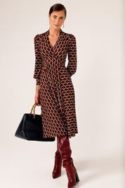 A model wearing the Auriga Dress in colour Ruby (Red), from the front, showing the whole outfit