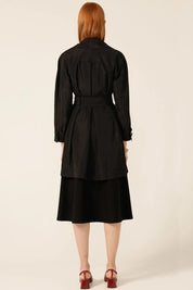 A model wearing the Noir Trench in colour Black (Black), from the back