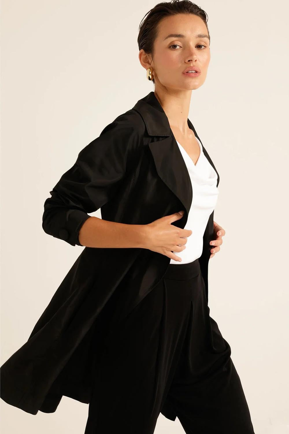 A model wearing the Noir Trench in colour Black (Black), from the front, cropped image