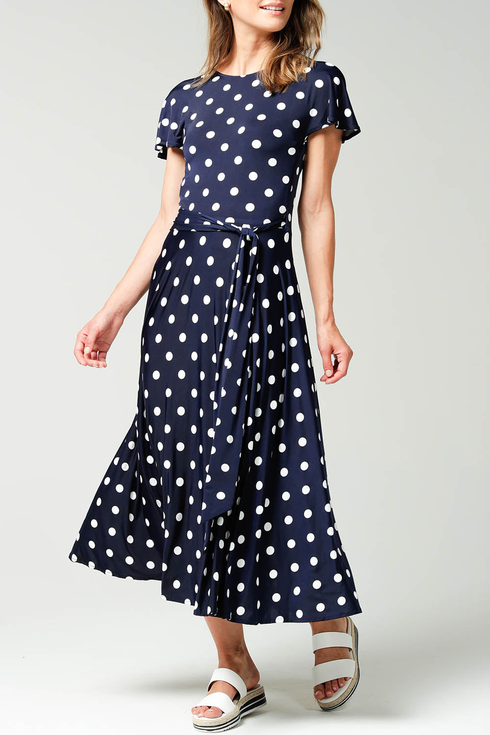 A model wearing the Reverse Wrap Midi Fluted Sleeve Dress in colour Polka (Blue), from the front, cropped image