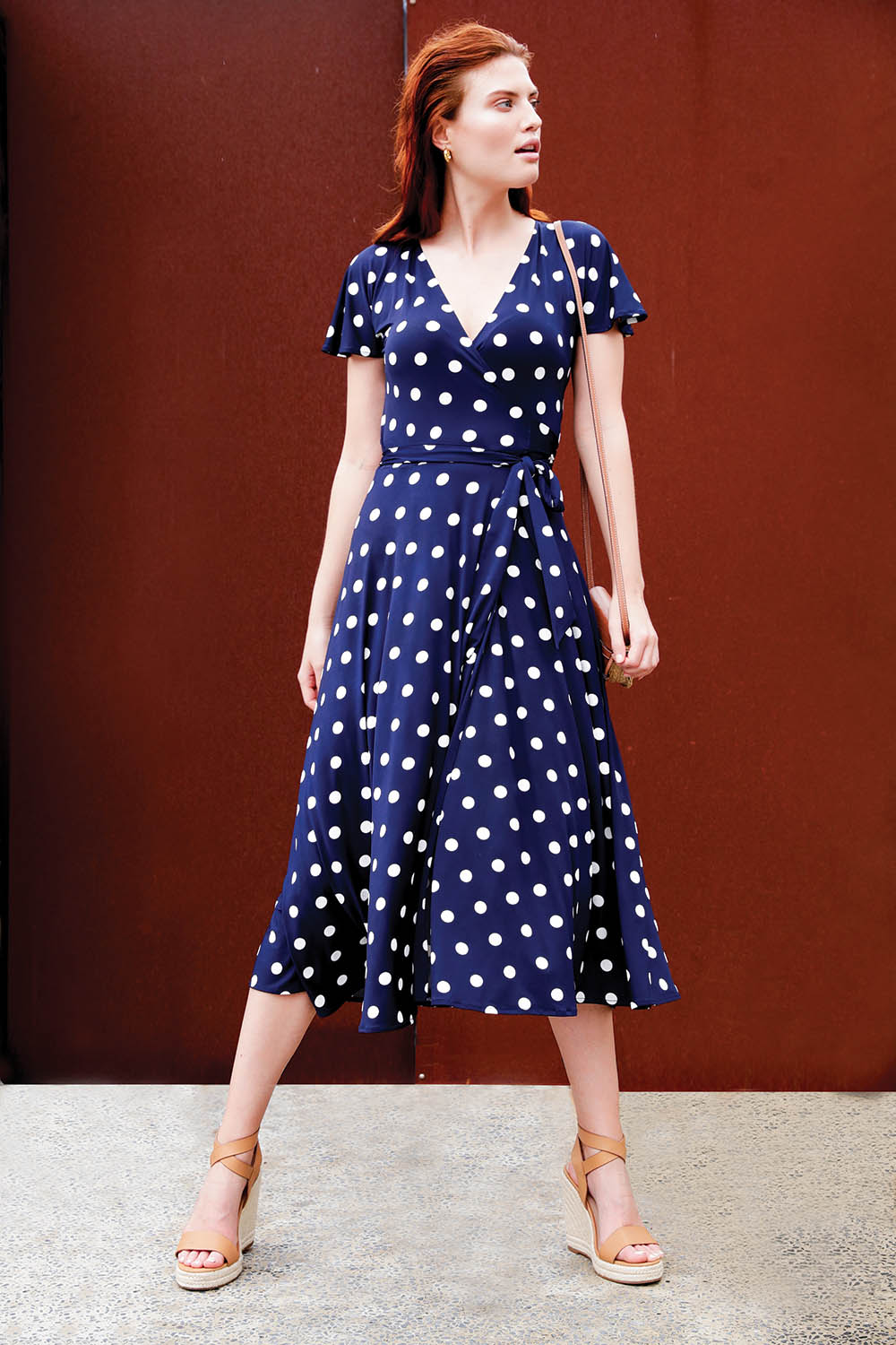 A model wearing the Reverse Wrap Midi Fluted Sleeve Dress in colour Polka (Blue), from the front, showing the whole outfit