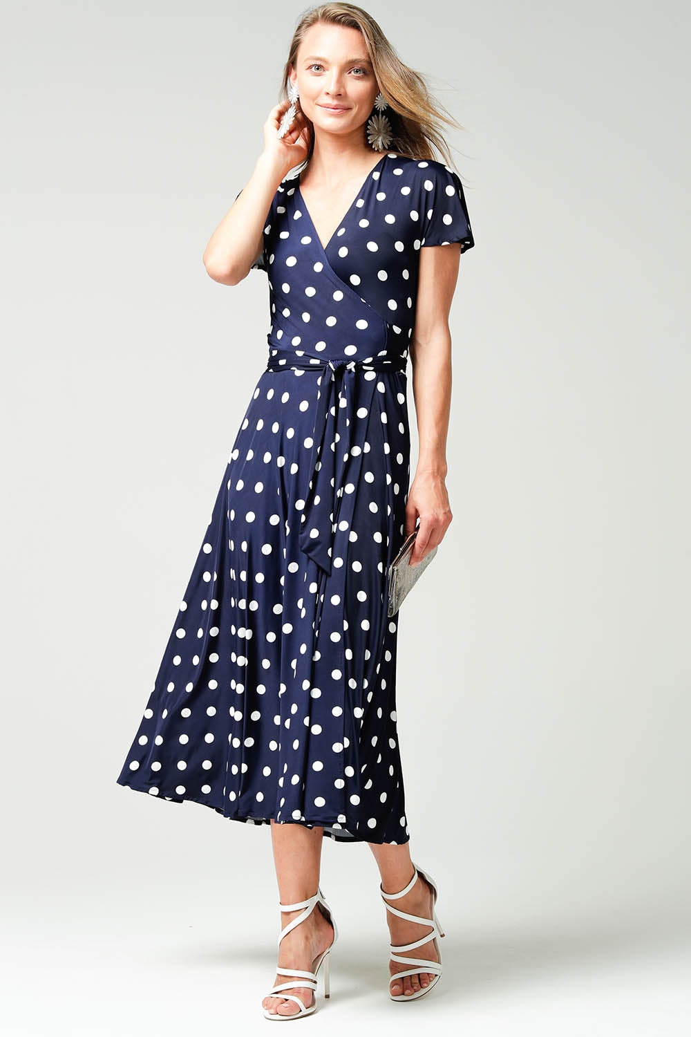 A model wearing the Reverse Wrap Midi Fluted Sleeve Dress in colour Polka (Blue), from the front, showing the whole outfit