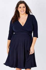 Model Mae wearing size 16 of the Reverse Wrap Full Skirt Dress in colour Navy (Blue), from the front, cropped image