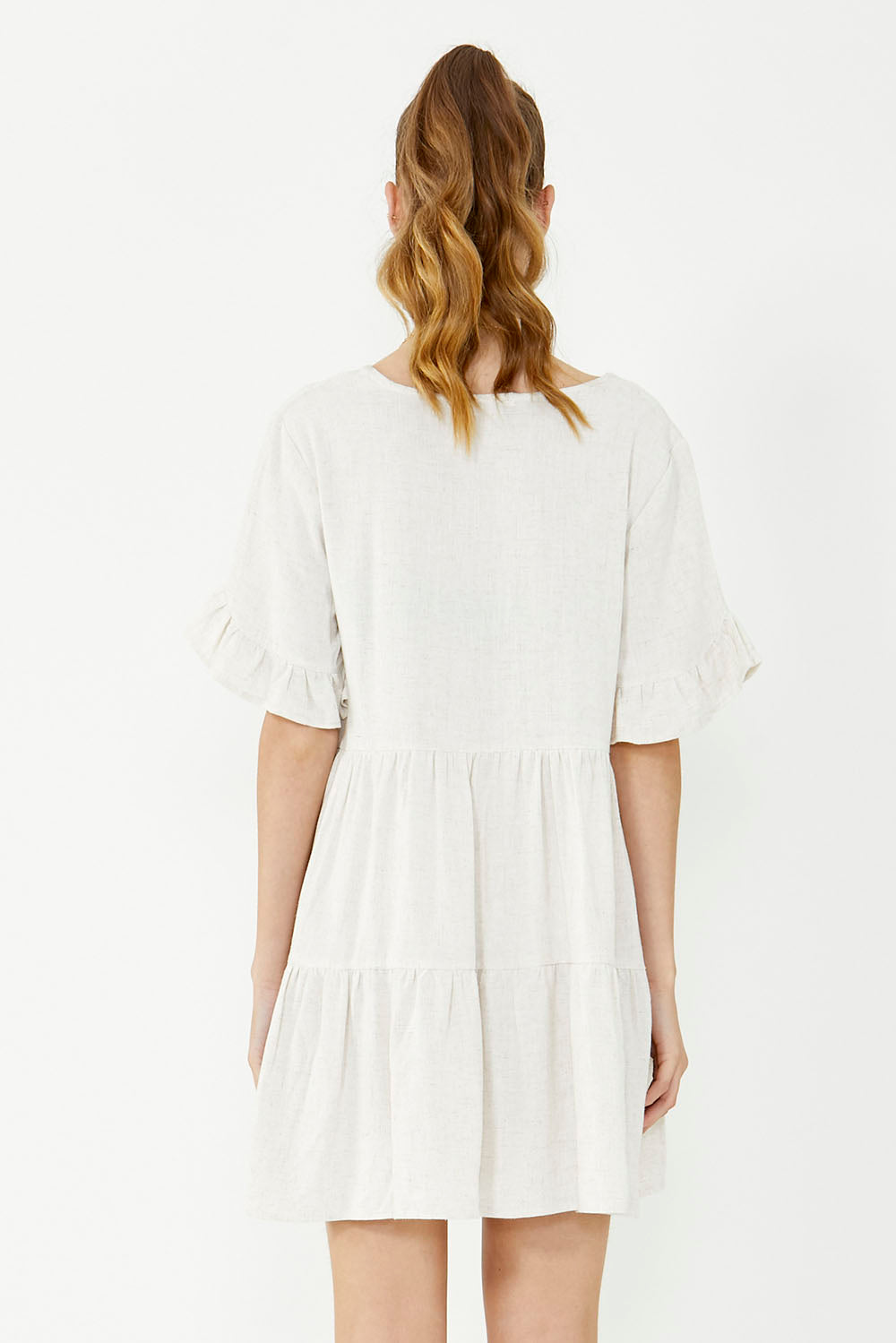 A model wearing the Gia Dress in colour Natural, from the back