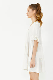A model wearing the Gia Dress in colour Natural, from the front, cropped image