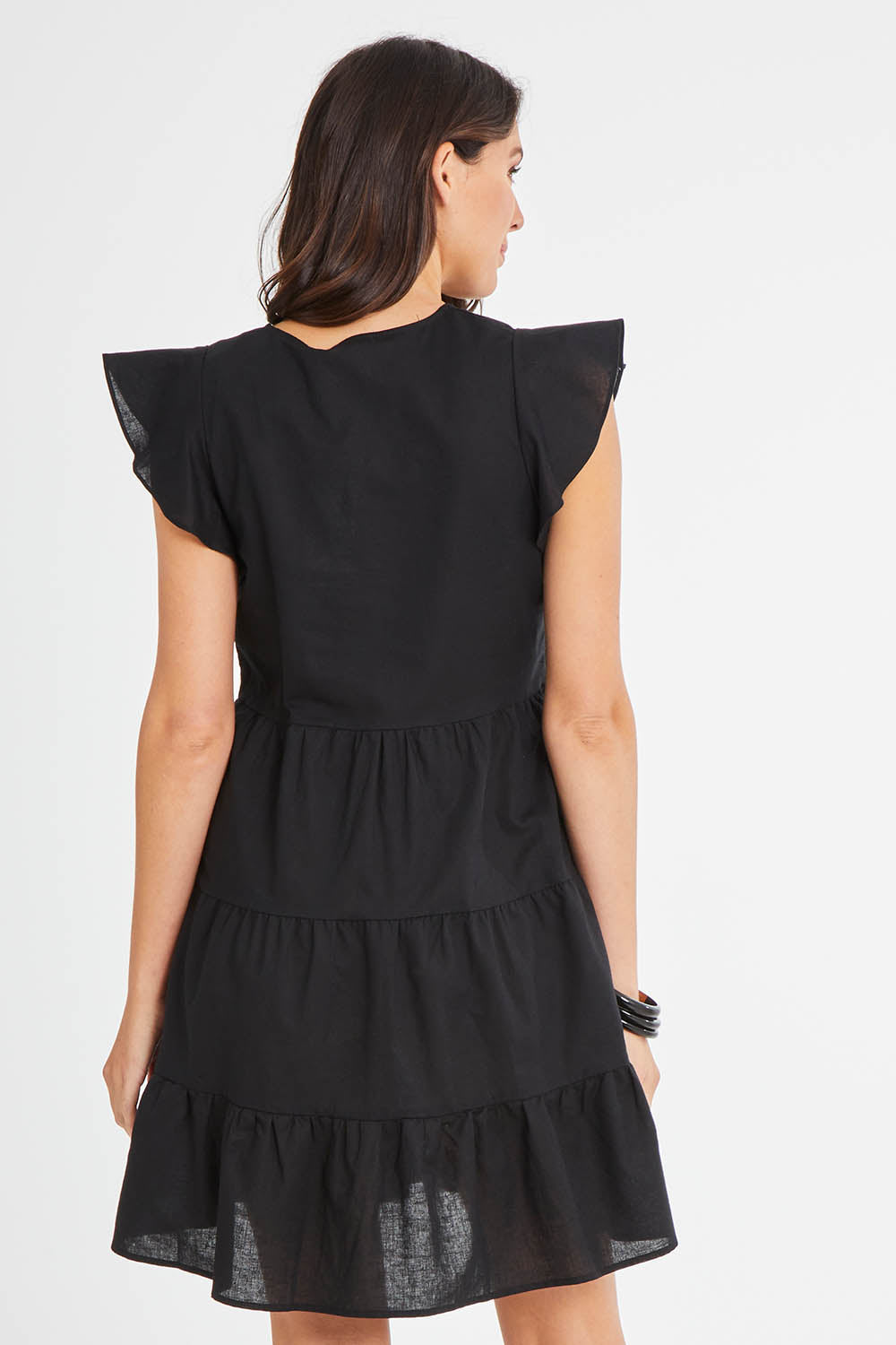 Model Madeline wearing size 10 of the Alina Tiered Linen Dress in colour Black (Black), from the back