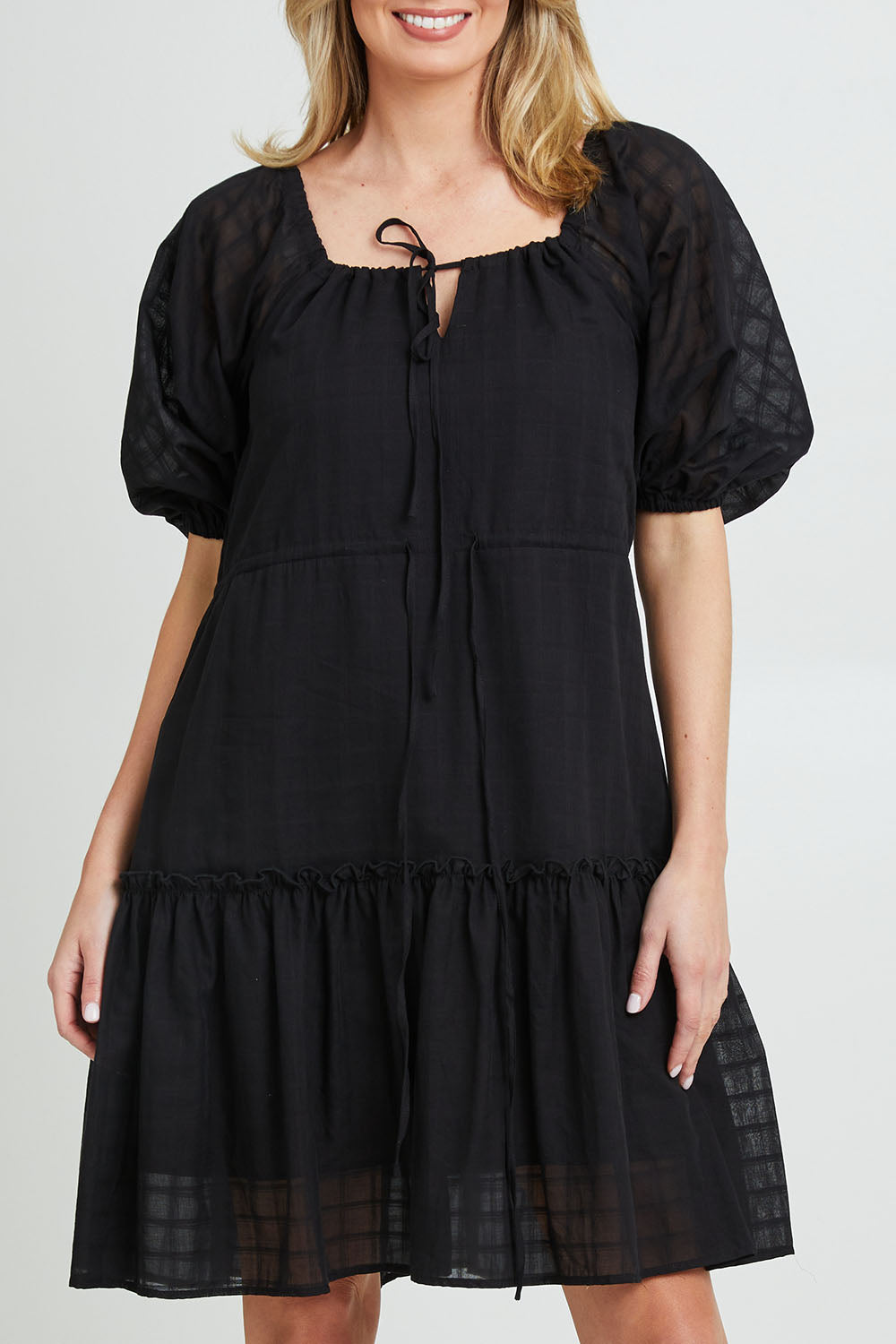 Model Grace wearing size 10 of the Ruby Tiered Midi Dress in colour Black (Black), from the front, cropped image