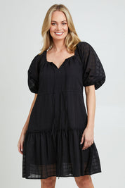 Model Grace wearing size 10 of the Ruby Tiered Midi Dress in colour Black (Black), from the front, cropped image