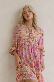 A model wearing the Chiara Dress in colour Paisley (Pink), from the front, showing the whole outfit