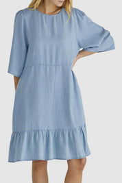 A model wearing the Rye Lyocell Dress in colour Chambray (Blue), from the front, cropped image