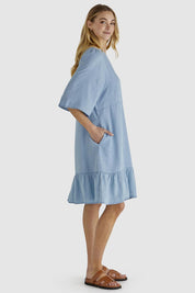 A model wearing the Rye Lyocell Dress in colour Chambray (Blue), from the front, showing the whole outfit