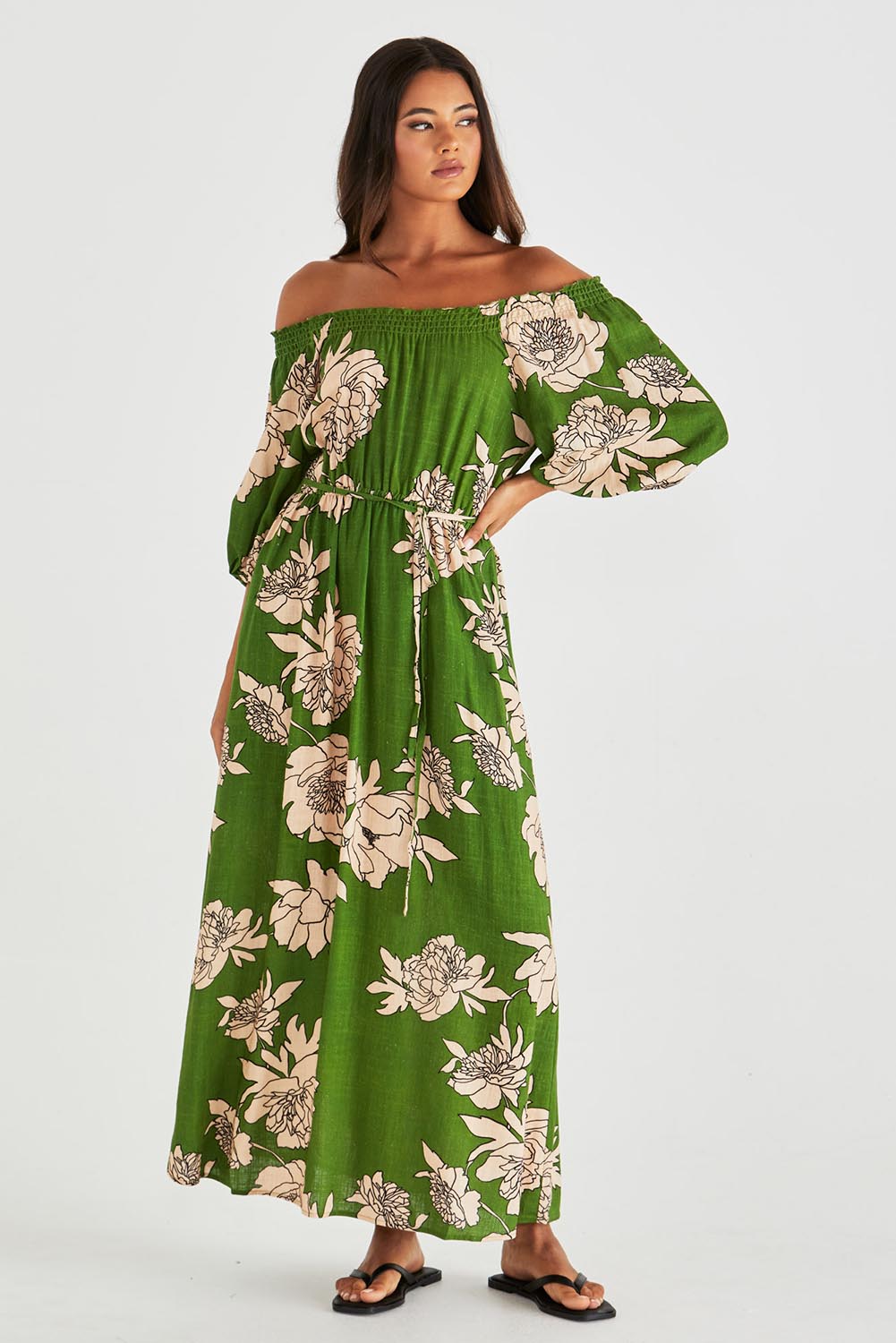 A model wearing the Antonie Off Shoulder Dress in colour Moonflower (Green), from the front, showing the whole outfit