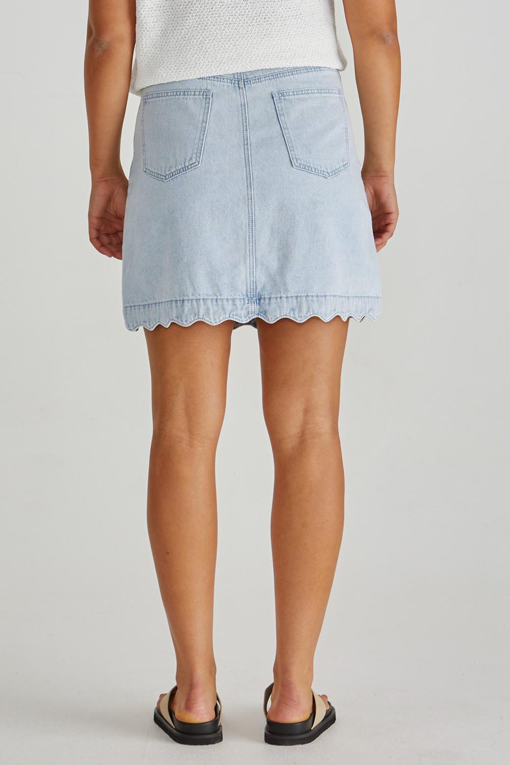 A model wearing the Vale Scalloped Denim Skirt in colour Bleach (Blue), from the back