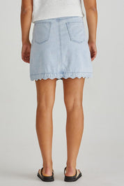 A model wearing the Vale Scalloped Denim Skirt in colour Bleach (Blue), from the back